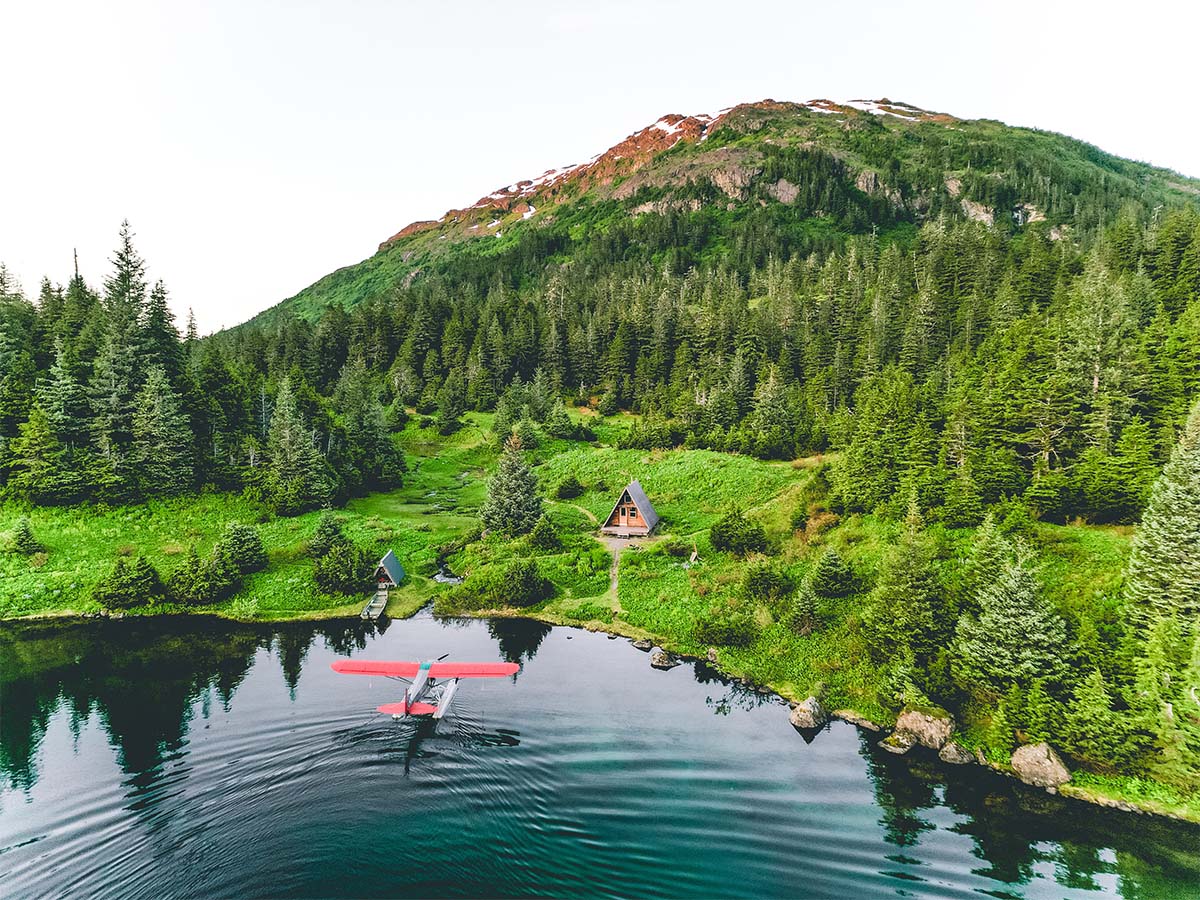 a forest service cabin on a lake with a float plane taxiing in on the water